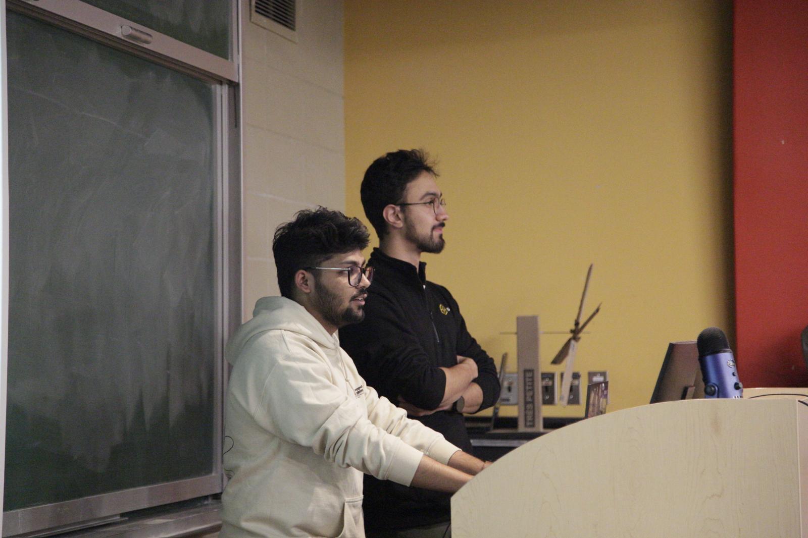 Two presenters at a lectern in front of a chalkboard